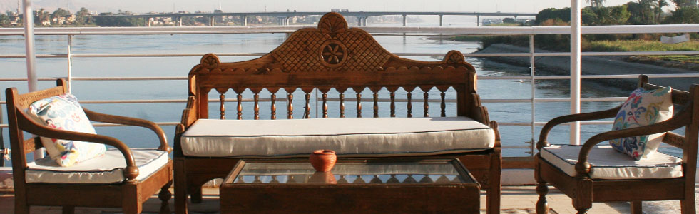 Wooden bench and chairs with cushions overlooking the Nile River aboard the M/S City & Sea Adonis.