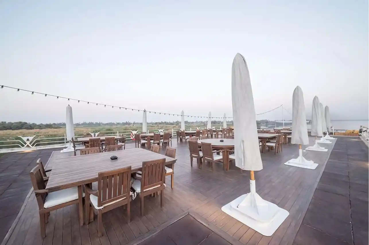 Sun deck dining area aboard the M/S City & Sea Adonis with wooden tables and white umbrellas overlooking the Nile River.