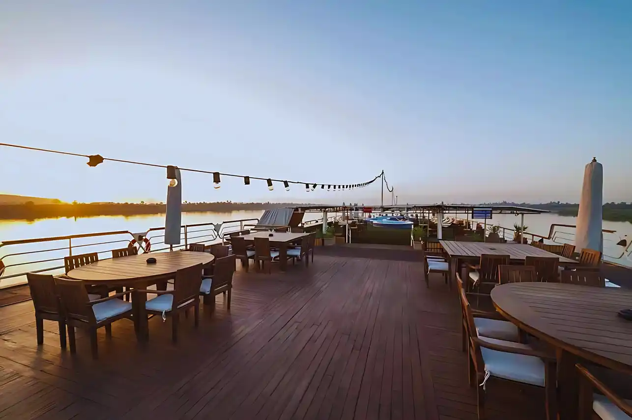 Sun deck aboard the M/S City & Sea Adonis with dining tables overlooking the Nile River at sunrise.