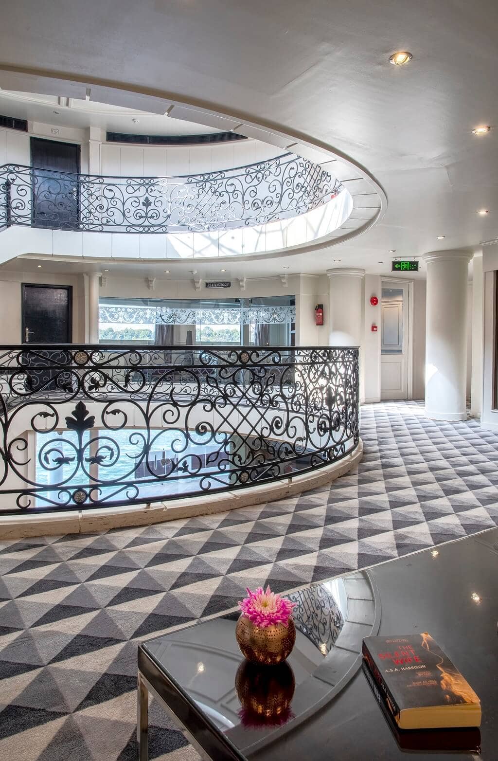 Elegant multi-level atrium aboard the M/S City & Sea Adonis with ornate wrought iron railings and geometric floor.